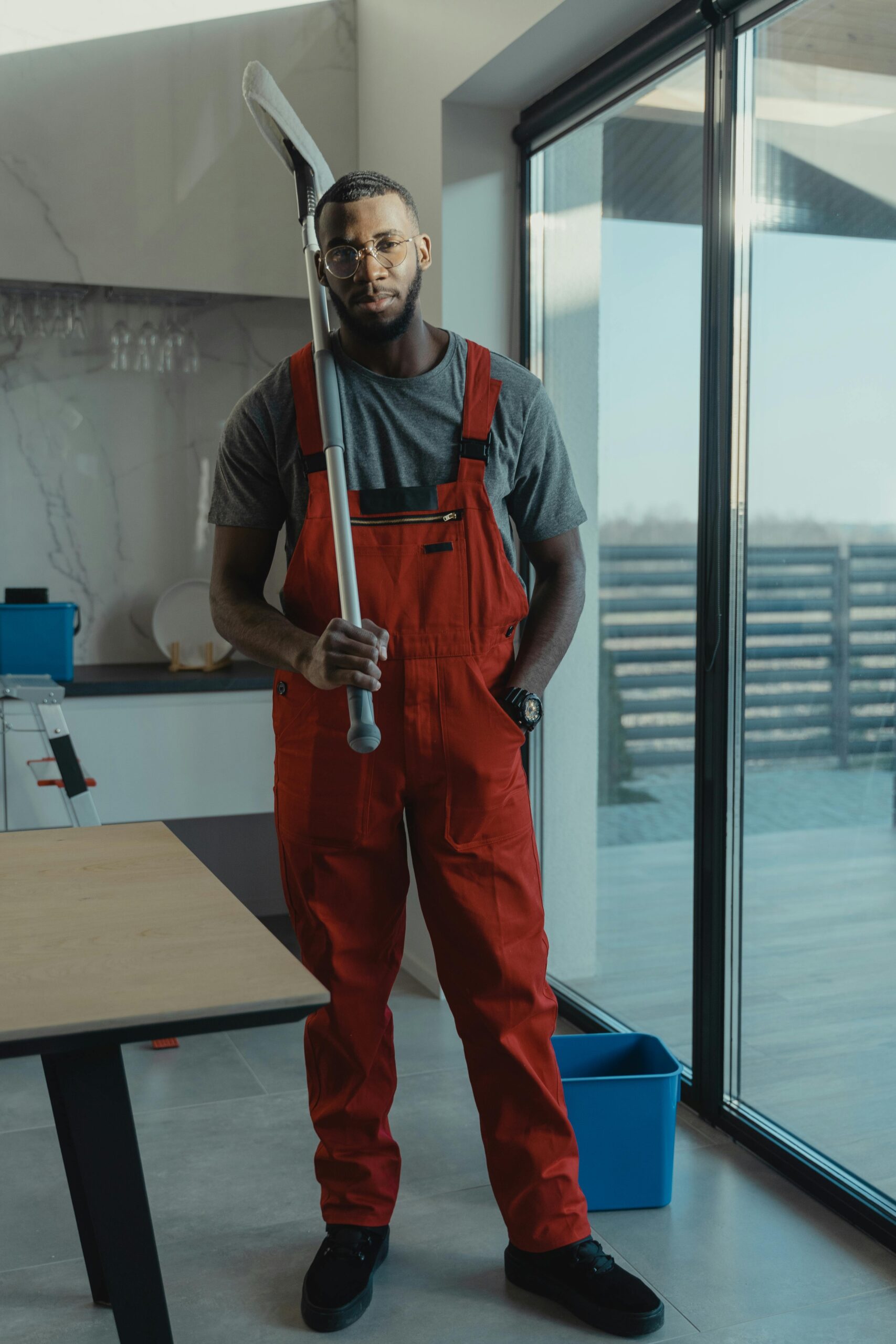 Portrait of a bearded worker in red overalls holding a mop indoors. Ideal for cleaning and home improvement themes.