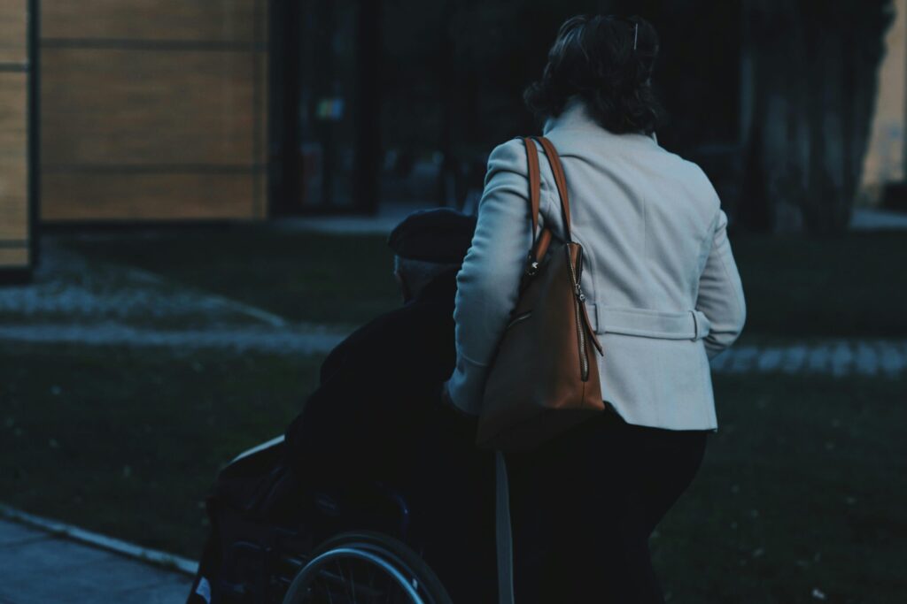 A woman assists a person in a wheelchair outdoors, demonstrating care.