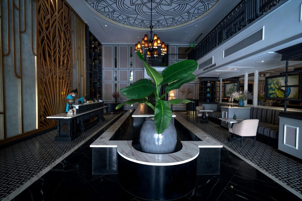 Luxurious hotel lobby featuring sleek decor, stylish chandelier, and central plant arrangement.