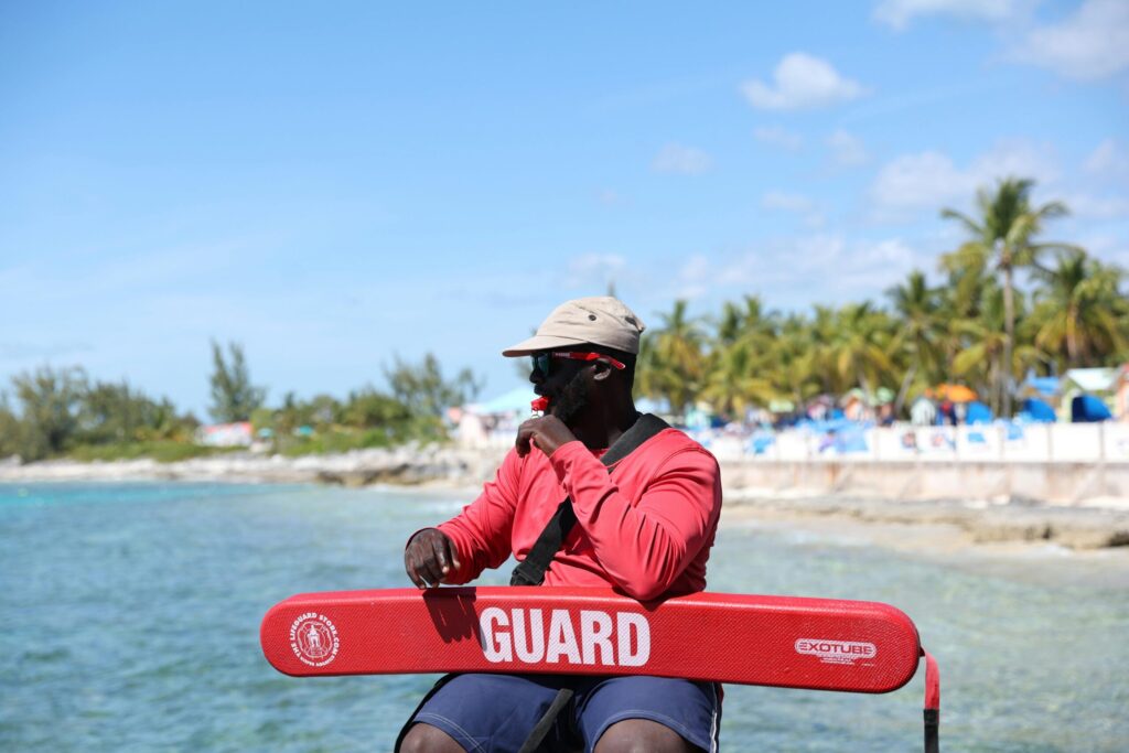 A lifeguard in red uniform sits at a tropical beach ready to ensure safety.