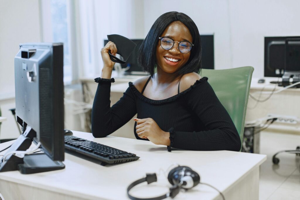 Smiling African American woman at office desk wearing glasses and black top.