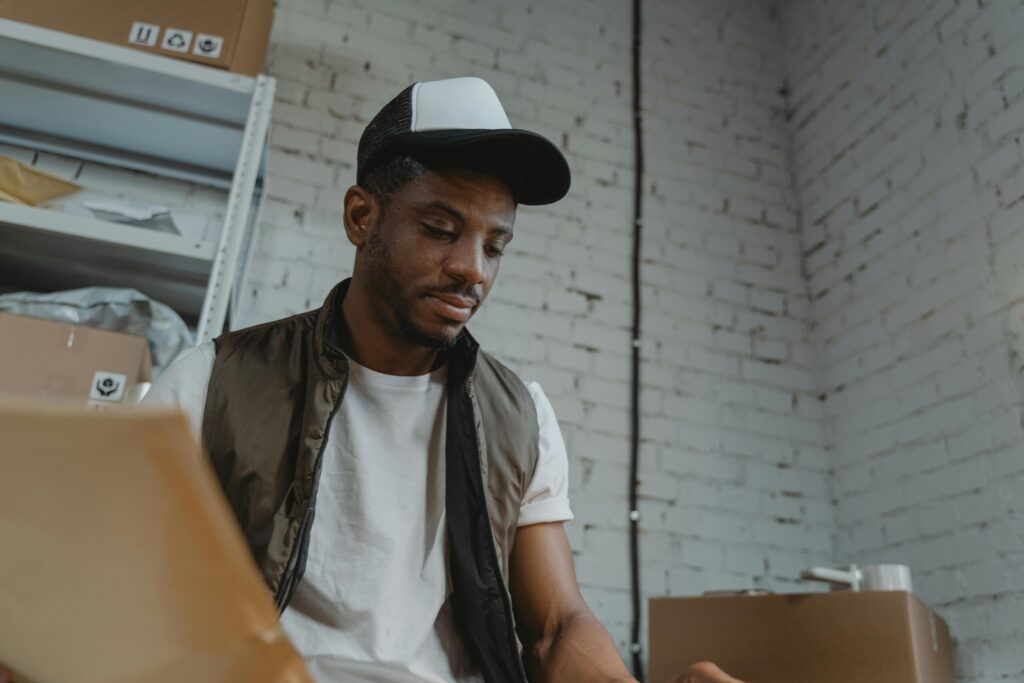 Man in a cap organizing packages in a warehouse with brick walls.