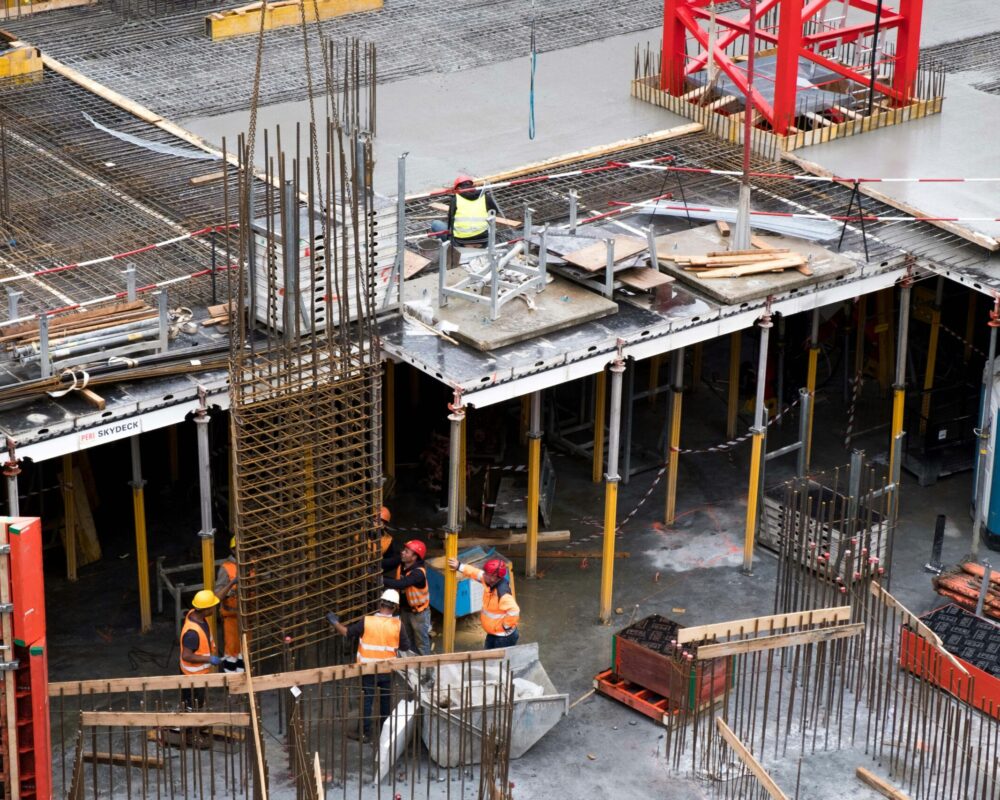 Workers in high visibility gear at a busy construction site with scaffolding and steel frames.